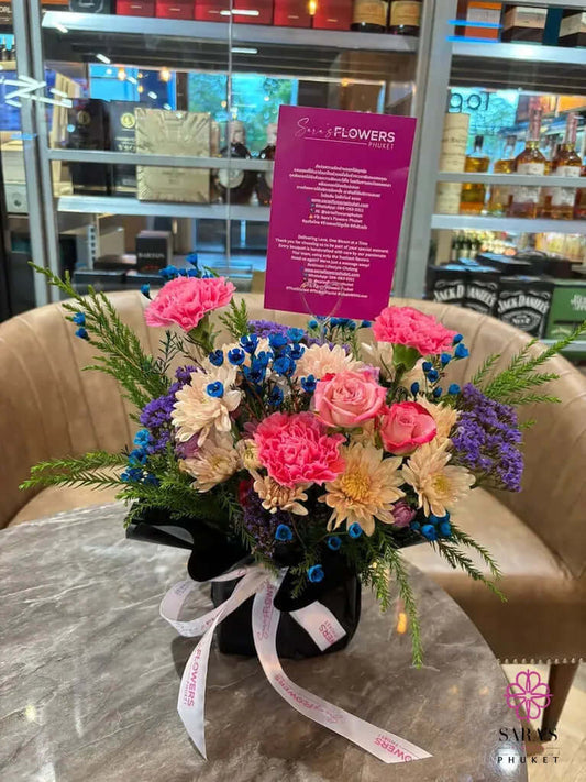 Colorful bouquet with pink carnations, blue baby’s breath, lavender statice, and black wrapping by Sara’s Flowers Phuket Same Day Delivery available.