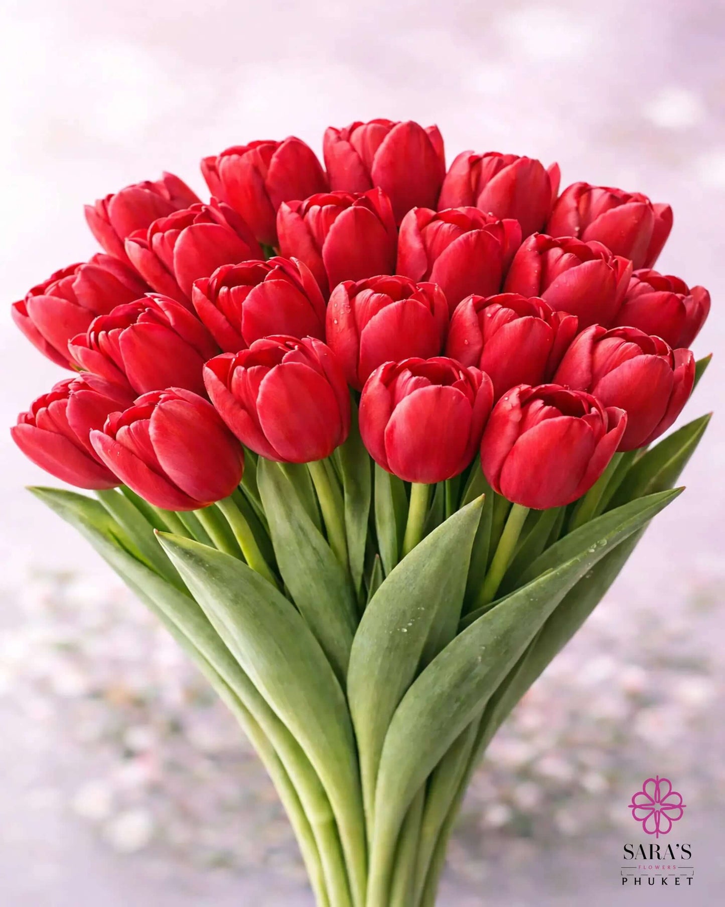 Vibrant red tulip bouquet with green stems, elegantly wrapped, featuring Sara's Flowers Phuket logo.