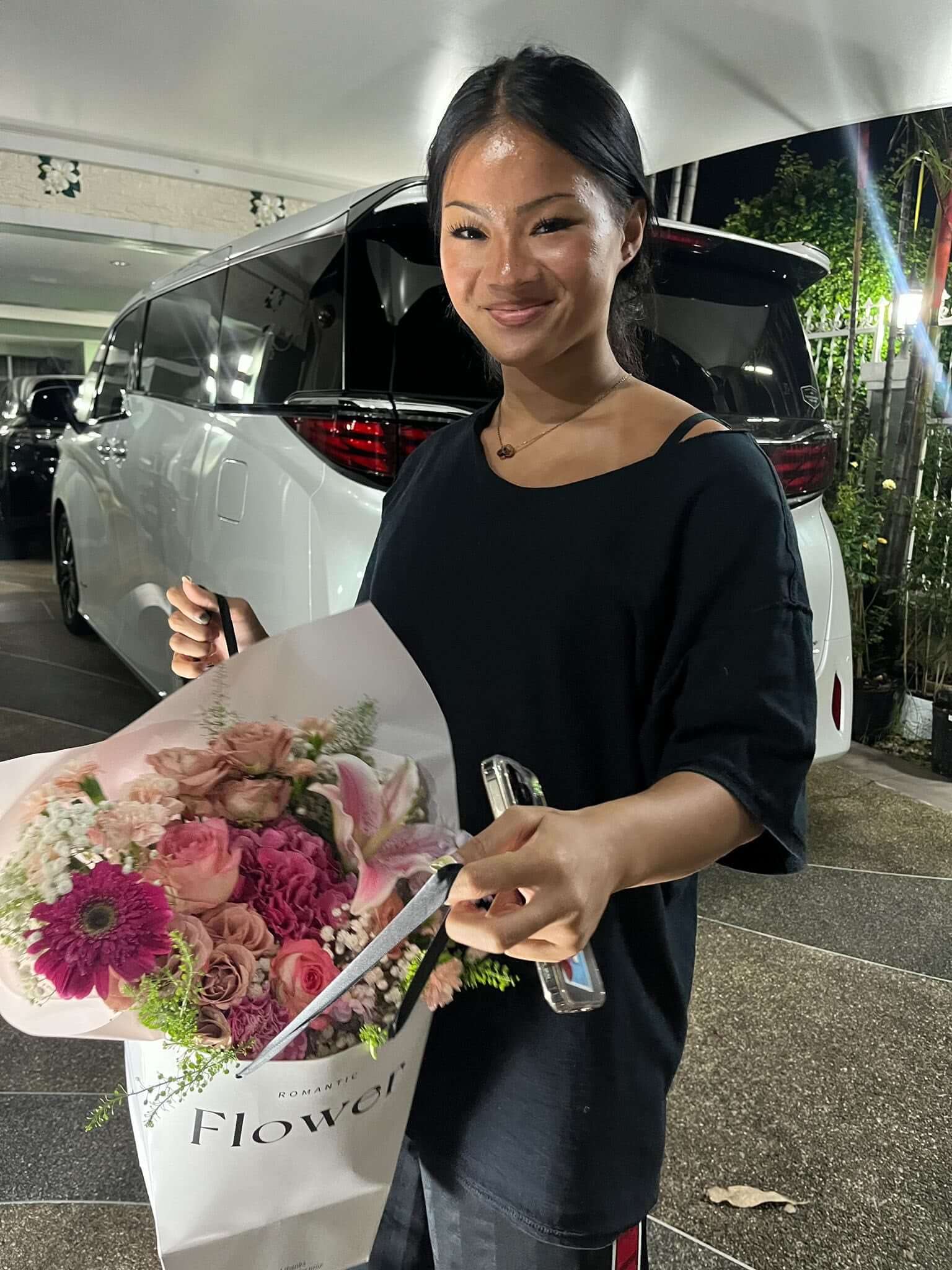 Woman holding a bouquet of flowers in front of a white limousine.
