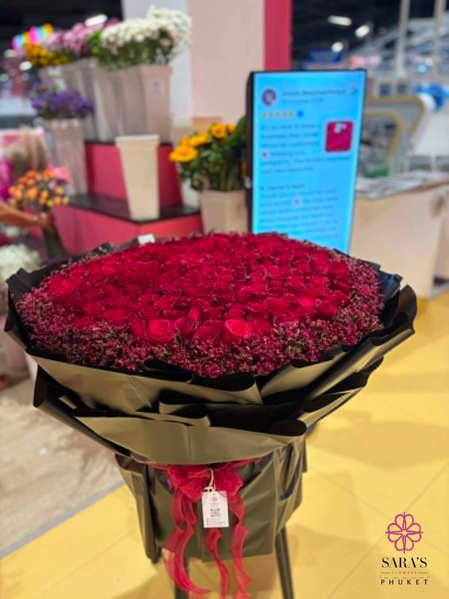 Bouquet of 200 red roses in a black wrap with a store interior in the background