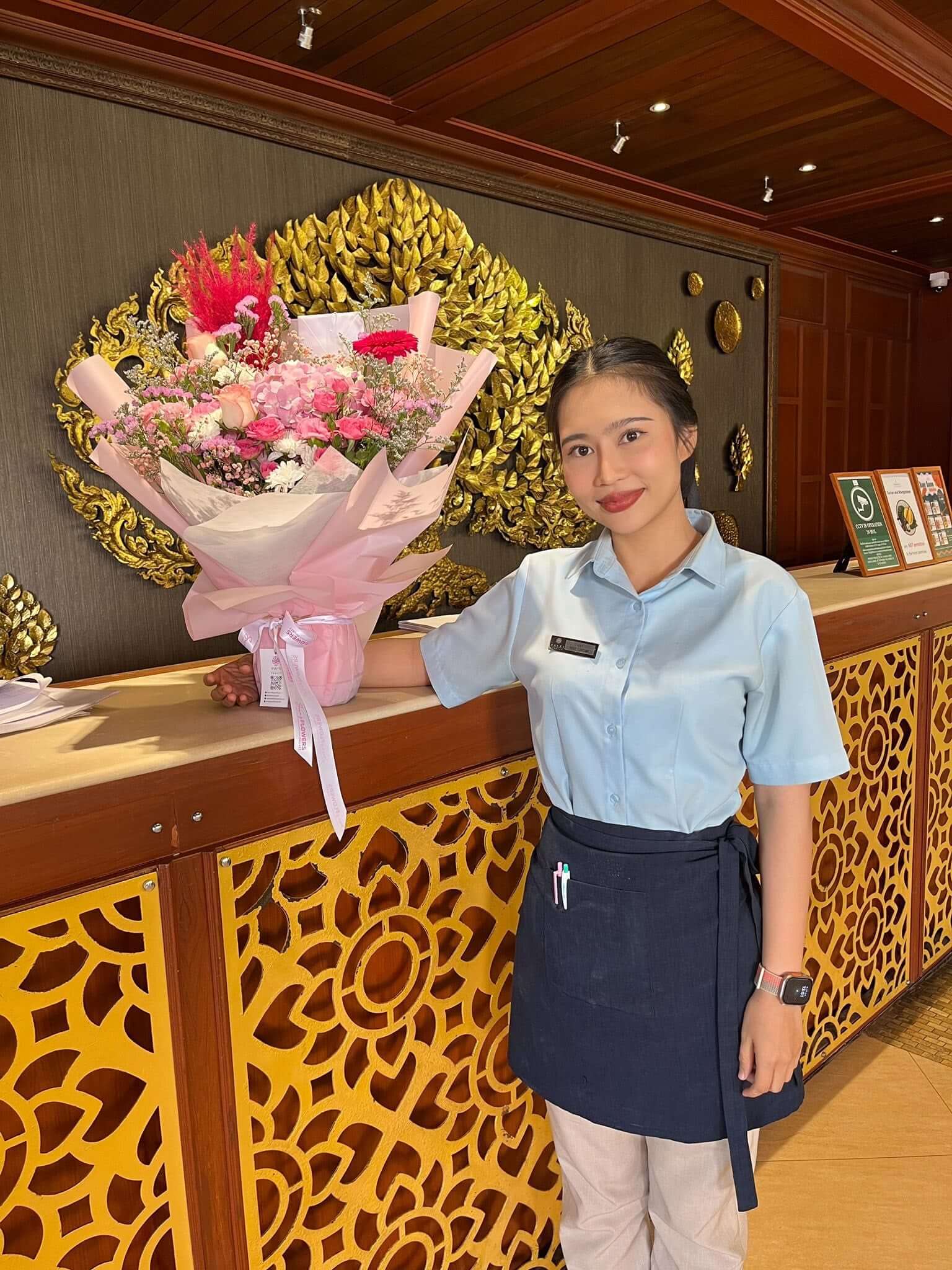 Person holding a bouquet of flowers in front of a hotel reception desk.