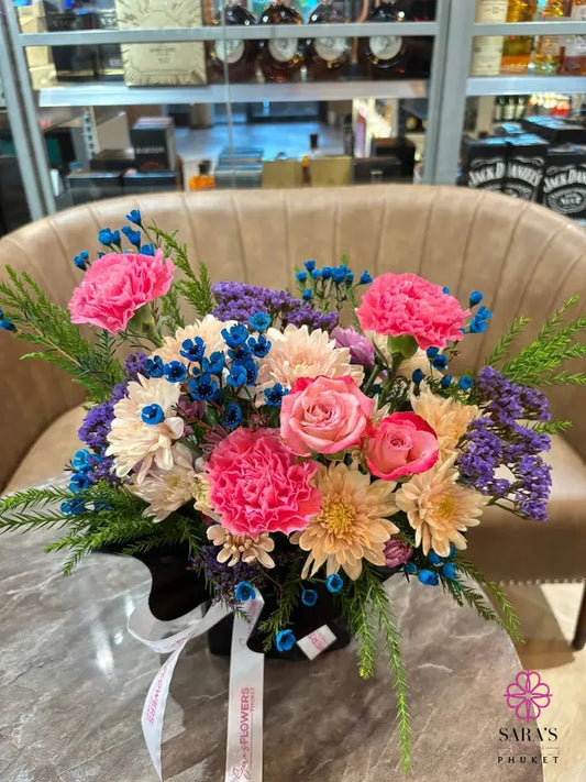 Colorful bouquet with pink carnations, blue baby’s breath, lavender statice, and black wrapping by Sara’s Flowers Phuket