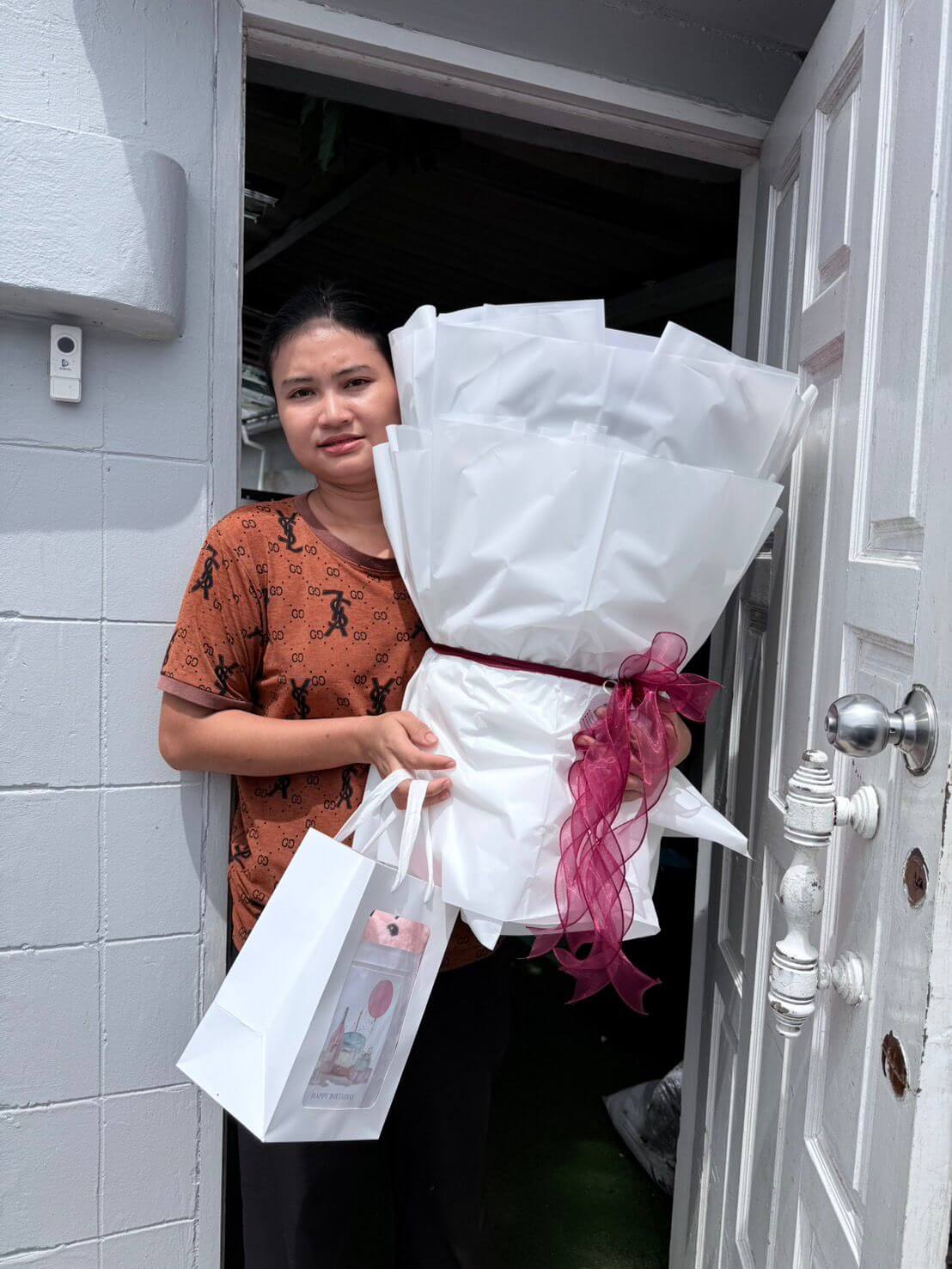 Woman holding a large bouquet of white flowers with a red ribbon and a smaller gift bag.