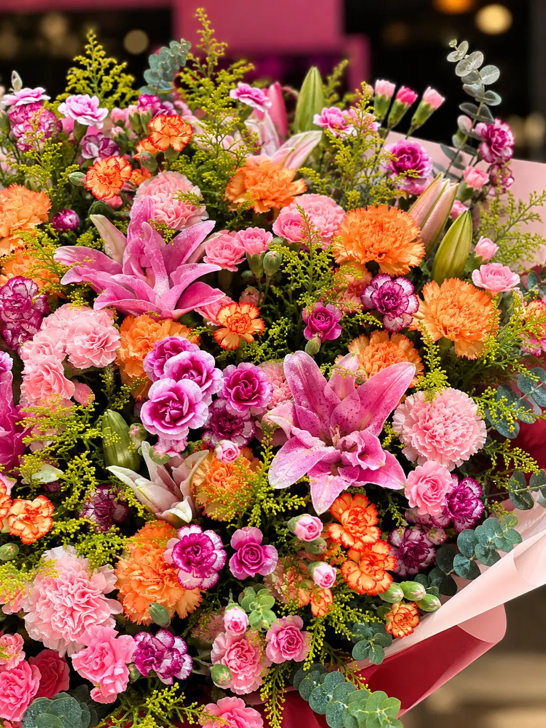 Close-up of The Grand Romance luxury bouquet featuring pink oriental lilies, peach and magenta carnations, eucalyptus and fresh greenery.