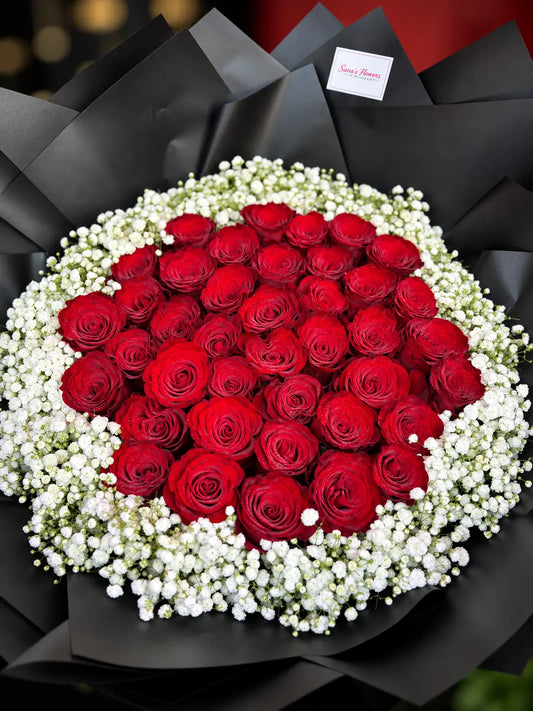 A bouquet of 39 red roses surrounded by white baby's breath, wrapped in black paper with a small card at the top.