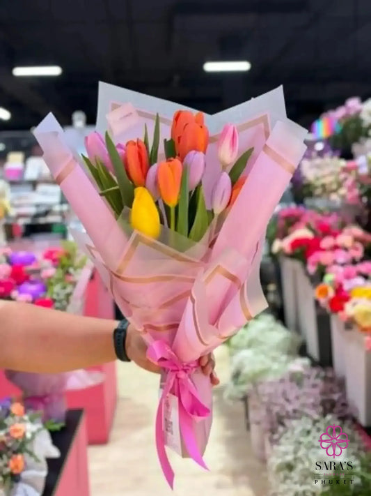 Hand holding Sara’s Signature Tulip Bouquet with colorful tulips in pink and white luxury wrapping.