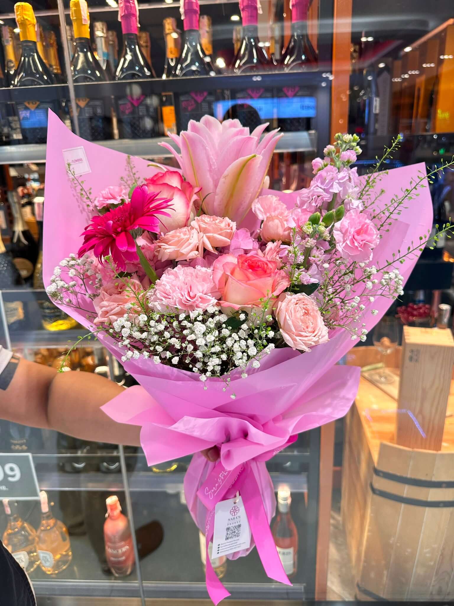 Bouquet of flowers wrapped in pink paper held in front of a store display.