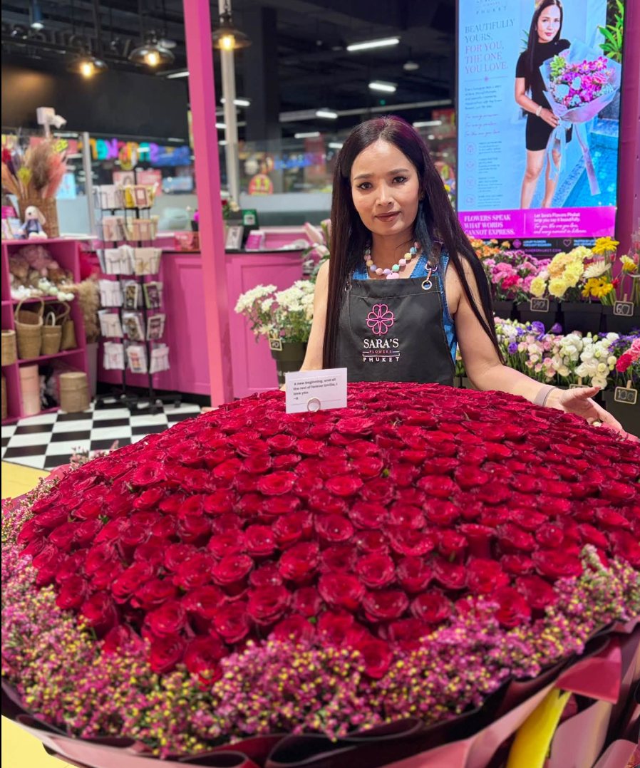 Eine Floristin in einer Schürze von Sara’s Flowers Phuket neben einem riesigen Strauß aus Hunderten roter Rosen