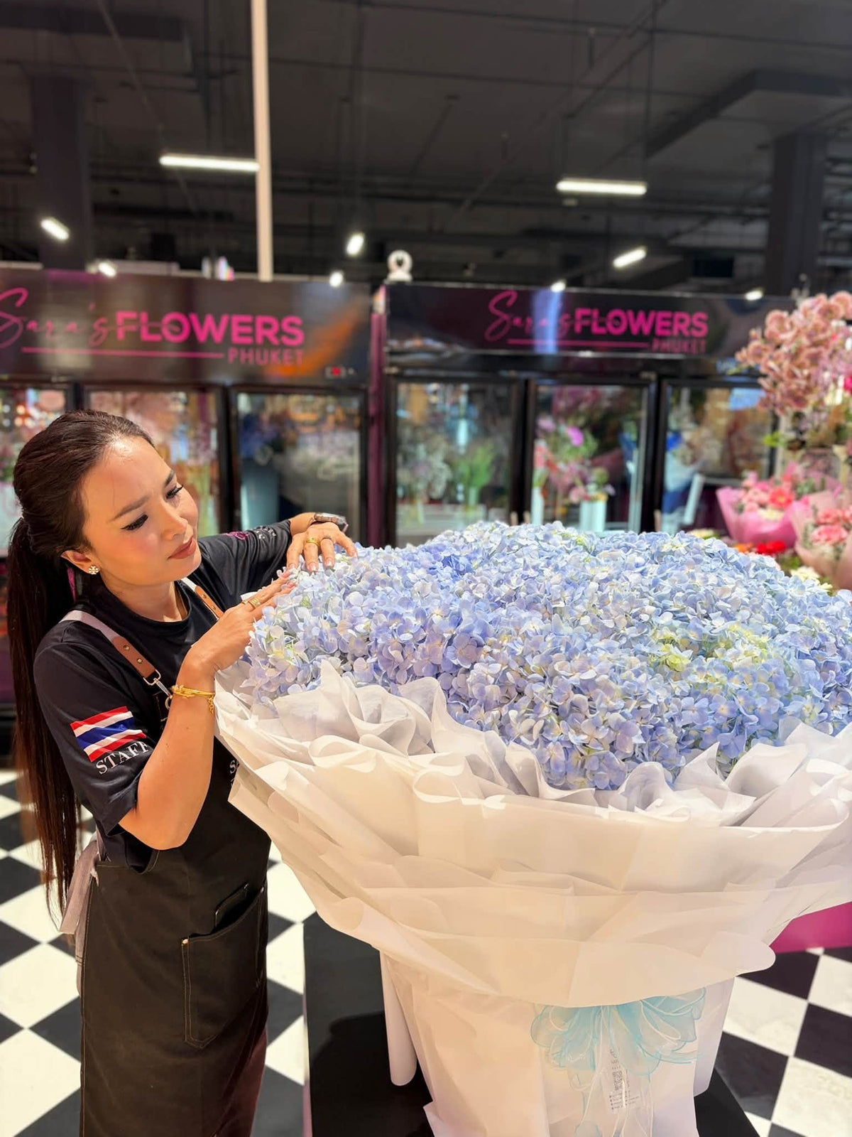 Sara arrangiert einen riesigen Strauß blauer Hortensien im Geschäft von Sara’s Flowers Phuket